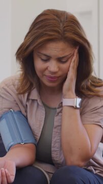 Vertical video: Touching temple during blood pressure check in clinic, woman wincing with cuff