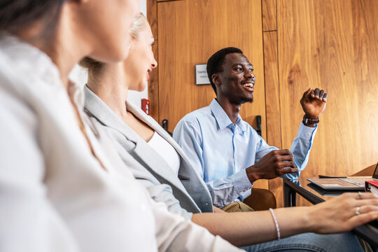 A group of young business people are sitting together in the office, brainstorming ideas and discussing future projects, while taking notes and sharing suggestions.