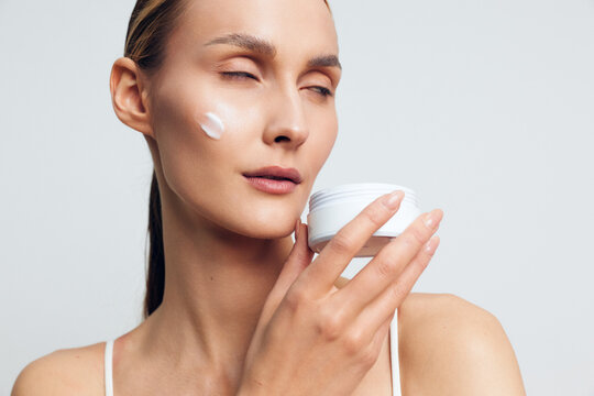 Woman skincare cream moisturizer on face, beauty portrait, calm hygiene in spa relaxation, light background, smooth skin texture, soft daylight, closeup beauty care