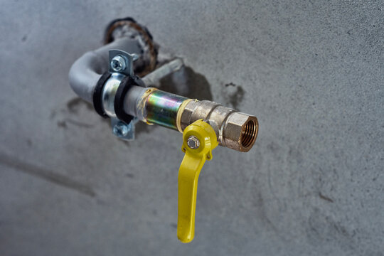 Close-up of a domestic gas pipeline installation featuring a brass ball valve with a yellow handle for safety control. Industrial setup is mounted on a concrete wall, representing utility services.