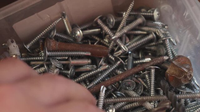 Close-up shot of a variety of screws and nails arranged in a disorganized pile, highlighting the diversity of construction fasteners in various sizes and shapes.