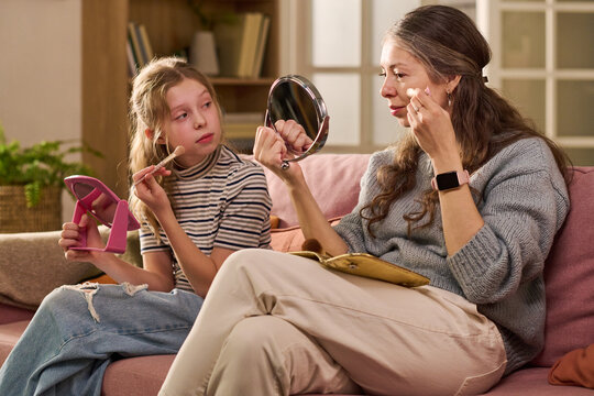 Caucasian mother and daughter applying makeup while sitting together, sharing beauty routine and bonding at home. Ideal for family lifestyle, parenting, skincare, self care marketing