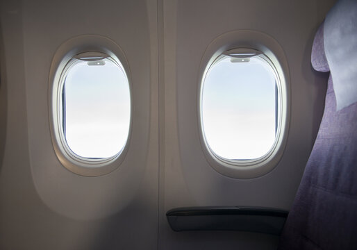 View of two airplane windows with a bright sky view and a purple passenger seat in the cabin Taiwan.