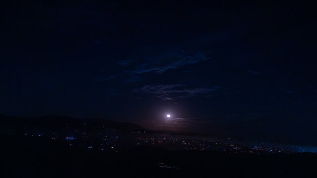 View of city lights twinkling in a valley under a bright full moon and dark night sky in Fallbrook, California, United States.