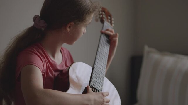 Young girl with long hair learning to play acoustic guitar at home. Portrait of young girl focused on learning guitar. Practice and musical education at home. Child leisure playing acoustic guitar.
