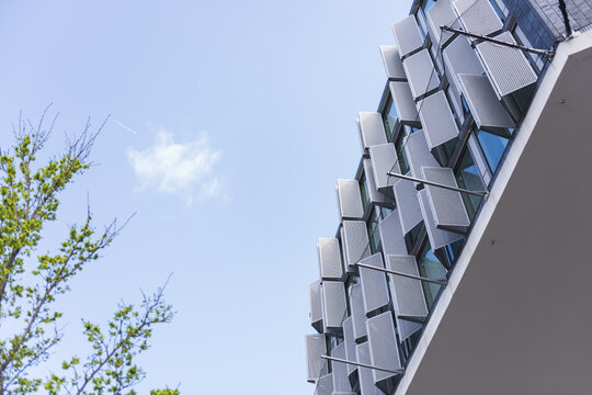 View of a modern building facade featuring perforated metal shutters against a clear blue sky with green tree branches in the Netherlands.