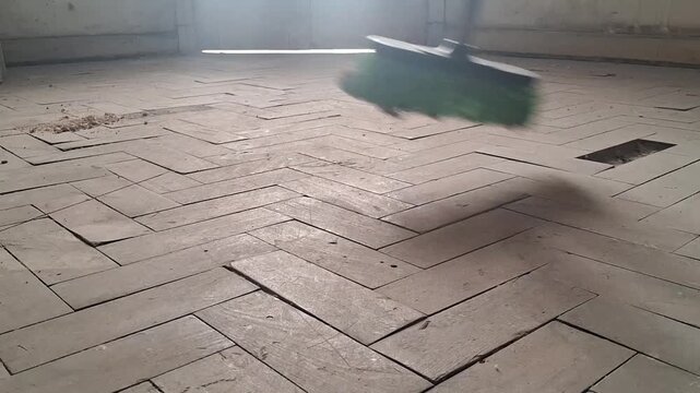 Bristled broom sweeping debris across vintage wooden parquet flooring in this cinematic slow motion video clip
