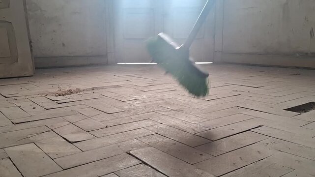 Sweeping dusty old herringbone wood floor with a green broom, illuminating particles in motion footage.