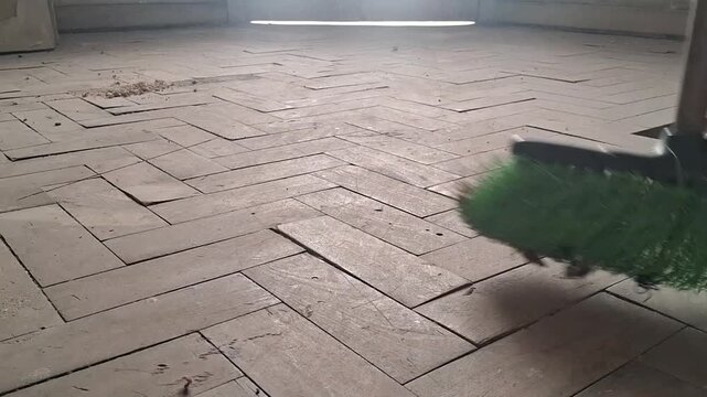 Green broom actively sweeping across a worn wooden herringbone floor in motion video