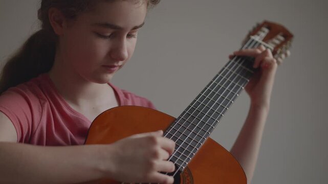 Young girl with long hair learning to play acoustic guitar at home. Portrait of young girl focused on learning guitar. Practice and musical education at home. Child leisure playing acoustic guitar.