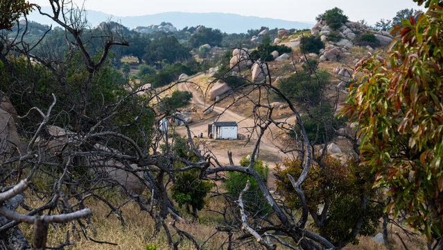 View of Splitrock Baby Oaks with large granite boulders, a small white shed, and winding dirt paths among dry brush and oak trees in Fallbrook, California, United States.