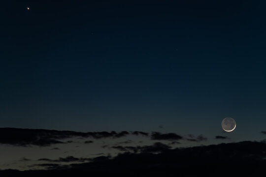 View of the crescent moon and a bright planet shining in the dark twilight sky above silhouetted clouds Kyiv, Kyiv city, Ukraine.