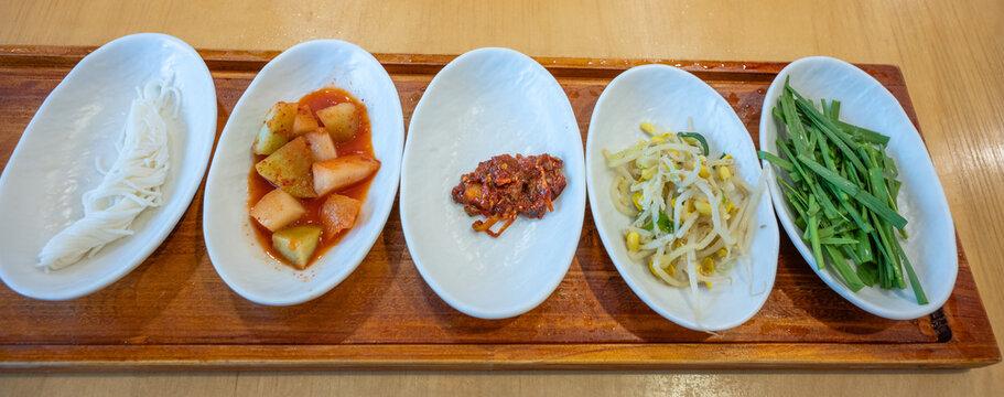 Assorted Korean side dishes banchan in white bowls on wooden tray