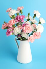 Naklejka premium Beautiful carnation flowers in vase on light blue background, closeup