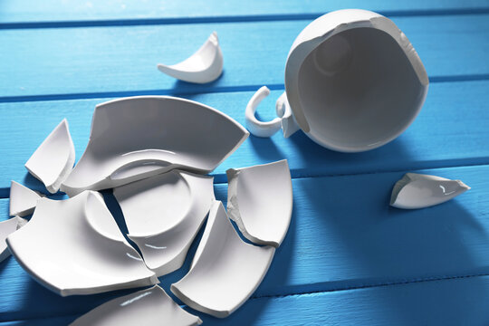 Pieces of broken saucer and cup on light blue wooden table, closeup