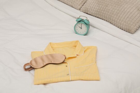 Alarm clock, sleeping mask and pajamas on bed, closeup