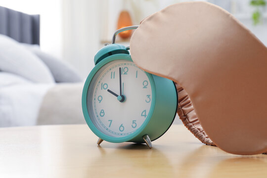 Alarm clock and sleeping mask on wooden table in bedroom, closeup. Space for text