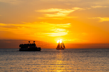 A sunset cruise and small sailboat silhouetted against the setting sun over a calm ocean.  © JHVEPhoto