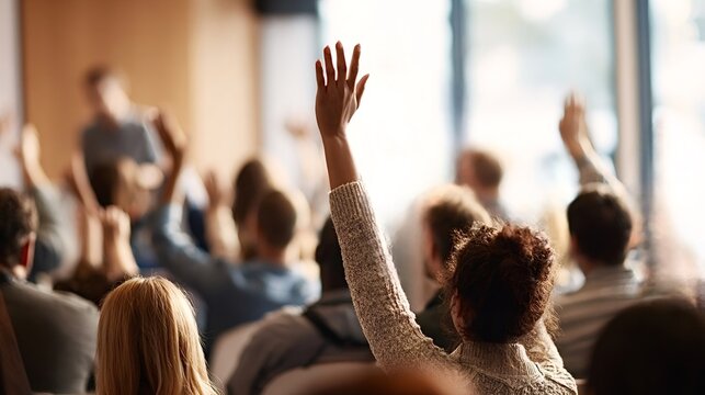 Diverse students attending a lecture or conference are actively participating, engaging with the speaker by raising their hands to ask questions or offer comments during an interactive session