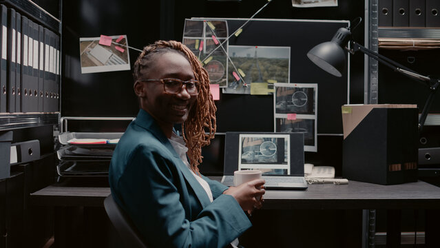 African american policewoman examining case files in evidence room. Female inspector analyzing surveillance information in folder and analyzing report, conducting criminal investigation.
