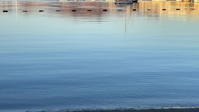 A tranquil sunrise over Bitez Bay, Bodrum. Sailboats rest on glassy, mirror like water, reflecting the golden light and coastal hills of the Turkish Riviera in a serene, panoramic view.