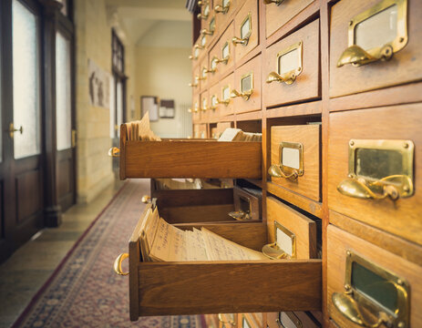 A vintage library card catalog with polished brass pulls and handwritten cards in a quiet academic hallway.