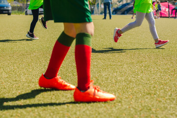 Fototapeta premium Young girls playing football on a sunny day, wearing bright green jerseys and colorful socks, with a well-maintained artificial turf field in the background