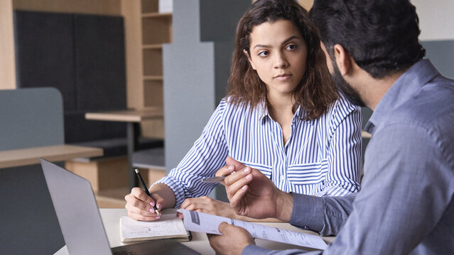 Mentoring young male Hispanic teacher and latin indian female student working together discussing course work. Insurance agent manager explaining conditions to client.