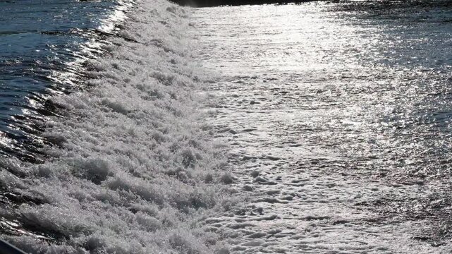 Water Flowing in a Weir and Creating White Foam with Bright Sun Reflecting