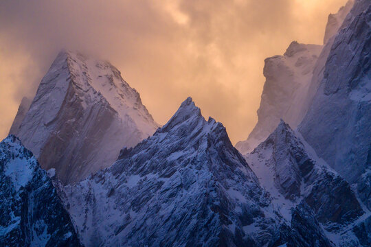 View of the sharp snow-covered peaks of the Haldi Cones under a dramatic golden sunset sky Khaplu, Baltistan, Pakistan.