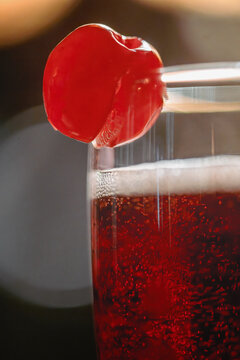 View of a sparkling red cocktail in a glass garnished with a maraschino cherry.