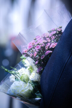 View of a person carrying bouquets of pink chrysanthemums and white roses wrapped in clear plastic.