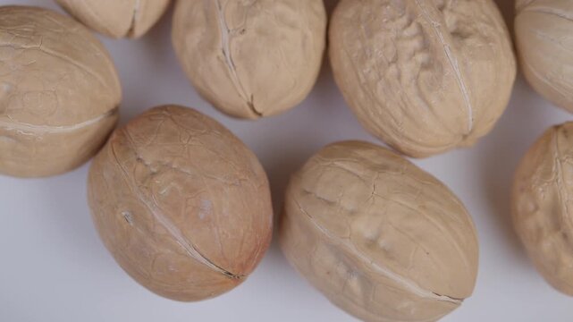 Walnuts on white. Unshelled walnuts displayed on white backdrop emphasizing texture. Detailed image of natural walnut shells with warm tones and minimal composition