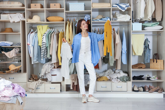 Woman choosing outfit near wardrobe with messy clothes indoors