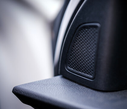 Macro focus on an interior black plastic door panel revealing a textured circular audio tweeter speaker grille installed inside a modern passenger vehicle cabin