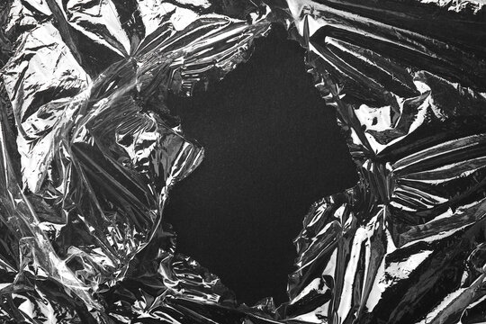 Torn plastic wrap on black background, top view. Space for text