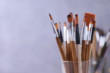 Fototapeta premium Paint brushes in glass on blurred background, closeup. Space for text