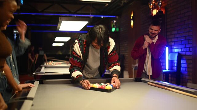 Young friends laughing and preparing for a game of billiards in a modern pool hall at night