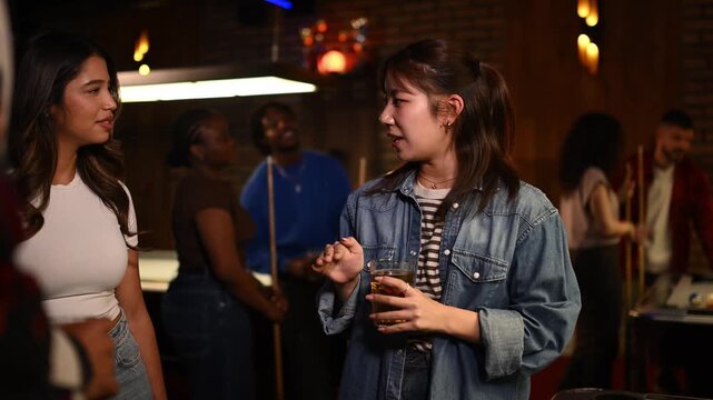 Asian and hispanic women chatting and drinking in a pool hall during a social gathering with friends