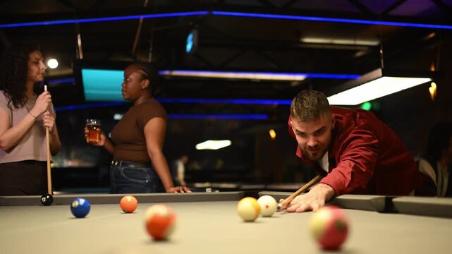Handsome man chalking cue stick and hitting cue ball playing pool game with friends in a billiard hall