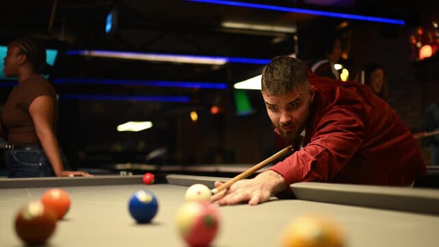 Handsome smiling man playing billiards making a winning shot and celebrating with friends in a bar