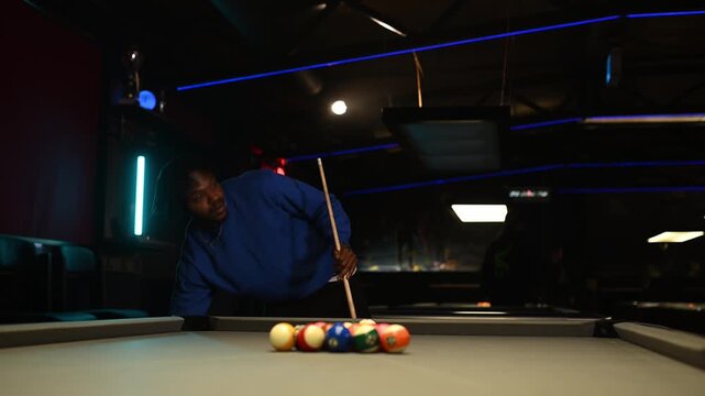 Young african american man racking pool balls and preparing to break the shot in a dark, neon lit billiards hall