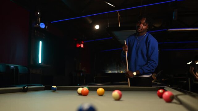 Focused african american man playing billiards and breaking the rack of balls in a dark, neon lit pool hall