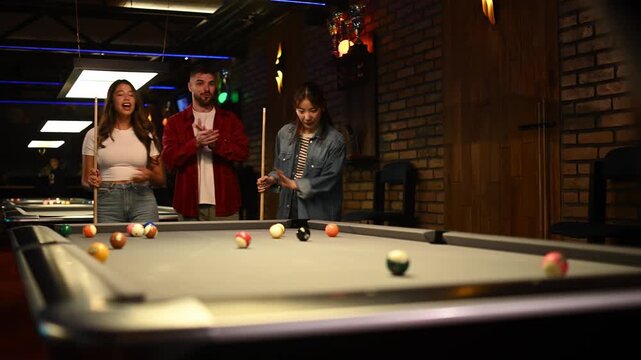 Excited group of multiracial friends watching a successful break shot while playing pool in a bar
