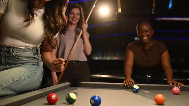 Three diverse female friends celebrating a successful shot while playing pool together in a dark club