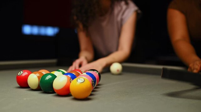 Two diverse young women setting up the triangle rack on a pool table. Close up on the colorful balls before starting the game in a pub