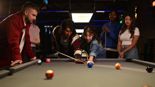 Young diverse friends enjoying a game of pool together while a woman successfully pockets a ball