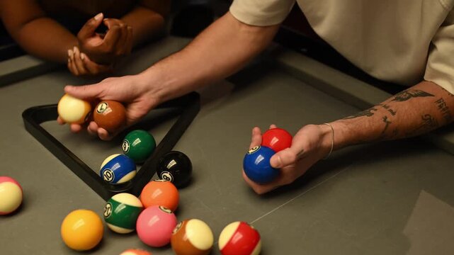 Two friends preparing for a friendly game of pool by racking the billiard balls on a grey table