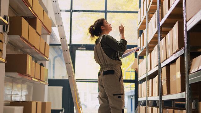 Young supervisor checking boxes logistics, working on quality control to ship retail store orders in warehouse. Female worker managing products packs with list of supply chain.