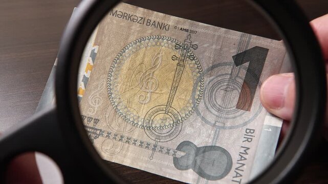 Examination of Azerbaijanian Manat cash money with magnfication glass, loupe. Concept of authenticity check, fight against counterfeiting of banknotes, anti fraud measures in Azerbaijan. Close up view